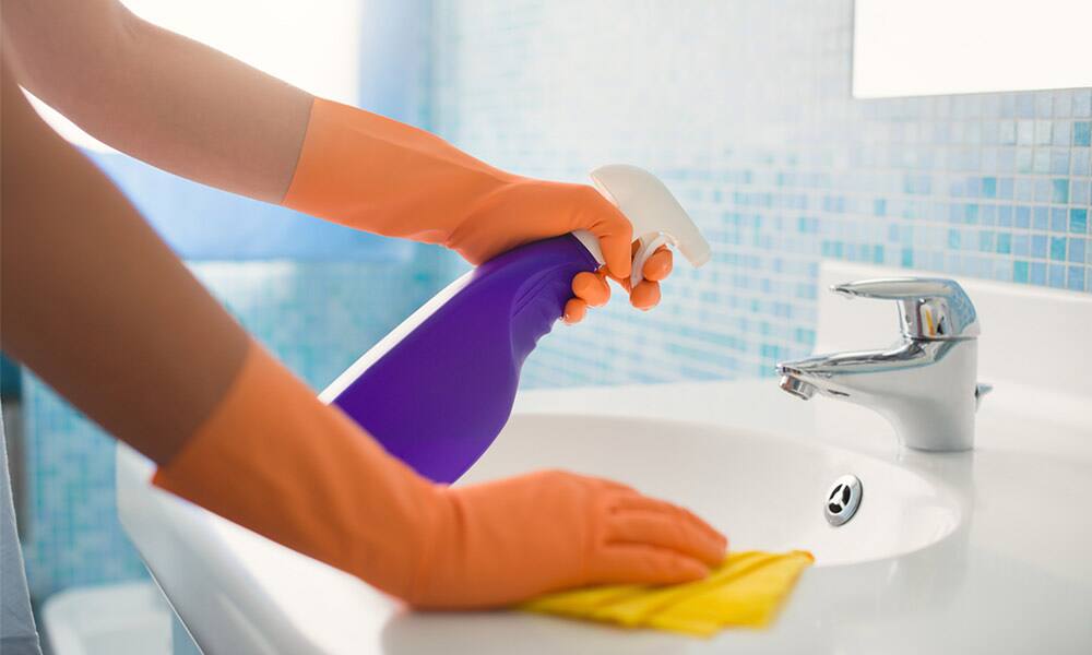 Gloved hand cleaning a bathroom basin and tap