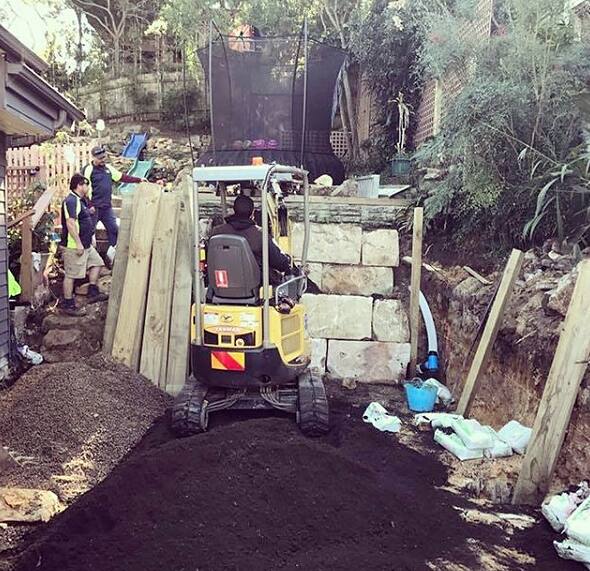 Compact excavator working on a tight-access sloping site with retaining walls