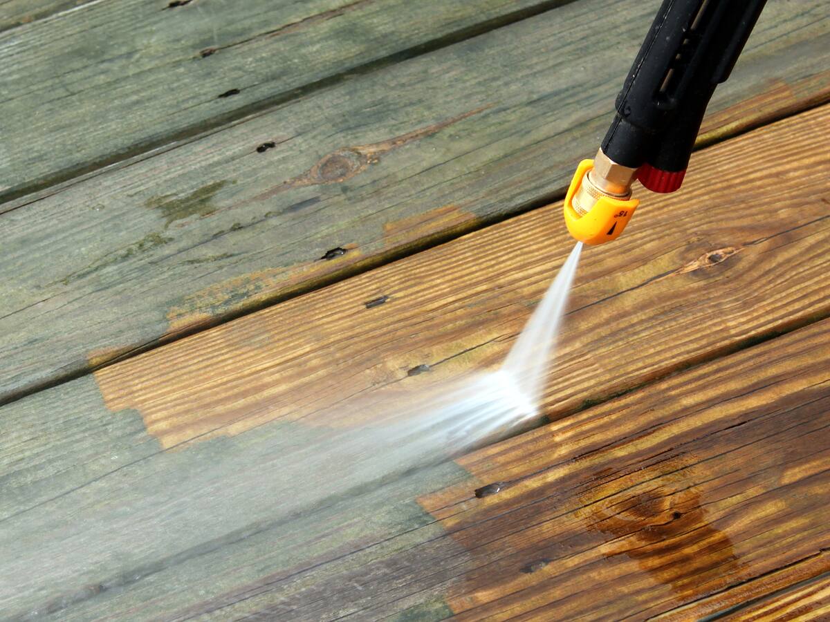 Pressure washer lifting grime off timber decking, showing the clean boards beneath